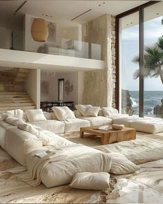 a living room filled with lots of white furniture next to a large glass window overlooking the ocean