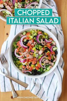 two white bowls filled with chopped italian salad on top of a wooden table next to silverware