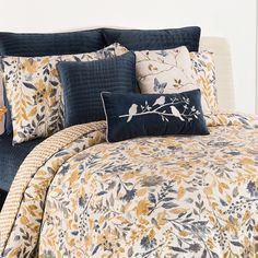 a bed covered in blue and yellow comforters with birds on the tree branch design