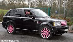 a black range rover with pink rims parked in front of a gated area