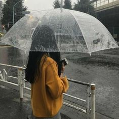 a woman is standing under an umbrella in the rain while looking at her cell phone