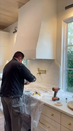 a man standing in front of a stove top oven next to a counter with tools on it