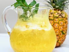 a glass pitcher filled with lemonade next to a pineapple on a white table