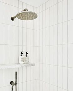 a shower head with two soap dispensers on it and a white tiled wall in the background