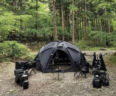 a tent set up in the middle of a forest with camera equipment on the ground