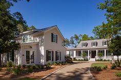 a large white house surrounded by trees and grass with a driveway leading to the front door