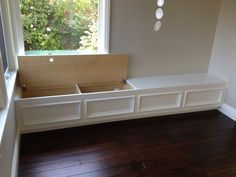 an empty room with wooden flooring and white painted furniture on the wall, in front of a window