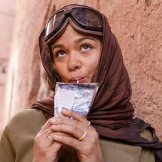 a woman wearing goggles and a headscarf holds up a piece of paper in front of her face