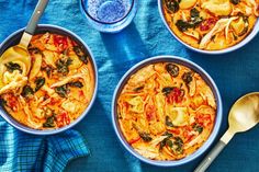 three bowls filled with pasta and spinach on top of a blue cloth next to silver spoons