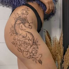 a woman's thigh with a dragon and flowers tattoo on her side, next to a wall