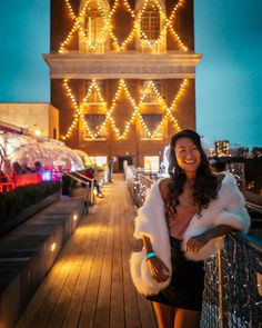 a woman standing on top of a wooden deck next to a tall building with lights