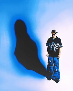 a man standing in front of a blue wall with his shadow cast on the wall