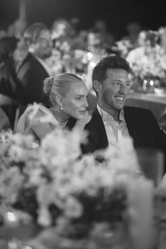 a man and woman sitting at a table with flowers in front of them, smiling