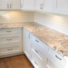 a kitchen with white cabinets and marble counter tops