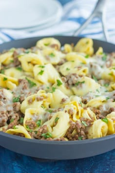 a skillet filled with pasta and meat covered in sauces on a blue table cloth