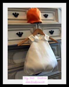 a baby's white shirt and orange hat hanging on a clothes hanger in front of an antique dresser