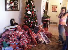 two girls standing in front of a christmas tree with presents piled on the floor next to it