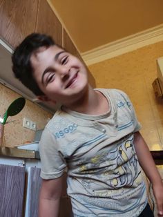 a young boy standing in the kitchen with a toothbrush next to him and smiling