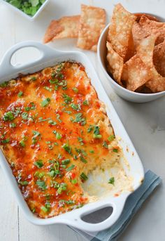 a casserole dish with cheese and vegetables next to some tortilla chips