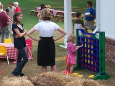 people are playing games in an outdoor area with hay bales on the ground and tables set up around them