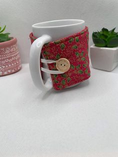 a white coffee mug with a red and green flowered design on the inside sits in front of two small succulents