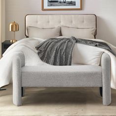 a bed with white linens and pillows in a neutral bedroom, next to a painting on the wall