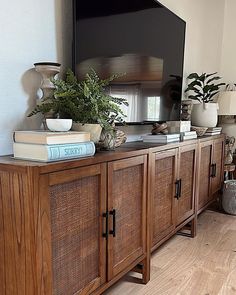 a flat screen tv sitting on top of a wooden cabinet next to a plant and books