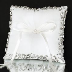 a white ring pillow with a bow on the front and ribbon at the back, sitting on a reflective surface