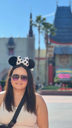 a woman wearing sunglasses and a minnie mouse ears headband in front of a building