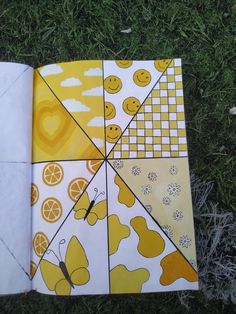 an open book with yellow and white designs on the pages, sitting in grass next to a pair of scissors