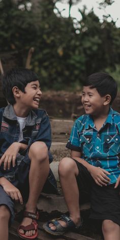 two young boys sitting next to each other on the ground smiling at each other with their feet crossed