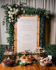 a wooden table topped with lots of pastries and desserts next to a sign