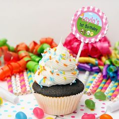 a cupcake with white frosting and sprinkles sits on a table surrounded by candy