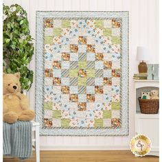 a teddy bear sitting next to a wall hanging on the side of a wall with a quilt