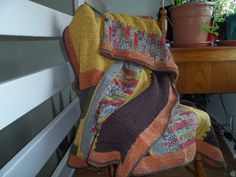 a chair that has a blanket on it and some potted plants in the background