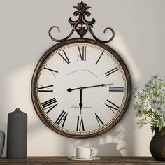 a clock hanging on the wall next to a vase with white flowers and a coffee cup