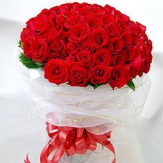 a bouquet of red roses in a clear vase with ribbon around the top and bottom