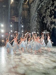 a group of dancers performing on stage with snow falling from the ceiling and lights behind them