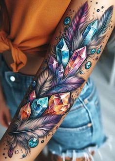 a woman's arm with a colorful feather and crystal stones tattoo on the arm