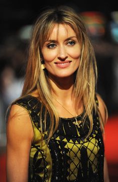 a woman with long blonde hair wearing a black and yellow dress smiling at the camera