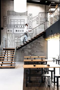 there is a man walking down the stairs in an empty room with tables and stools