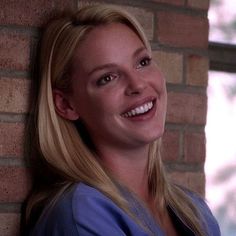 a woman leaning against a brick wall with her arms crossed and smiling at the camera