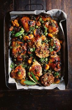 a pan filled with chicken and vegetables on top of a wooden table