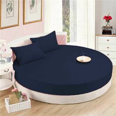 a round bed with blue sheets and pillows in a room next to a white chair