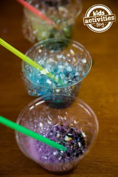 three cups filled with different colored liquid and straws on top of a wooden table