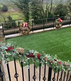 christmas wreaths on the railing of a house with green grass and trees in the background