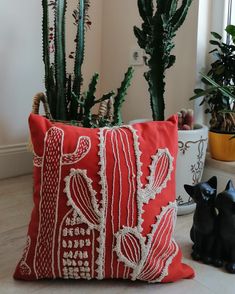 a red pillow sitting on top of a white floor next to a potted plant