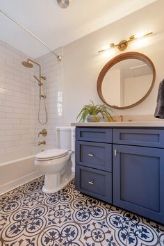 a white toilet sitting next to a bath tub in a bathroom under a round mirror