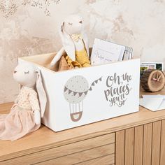 a stuffed animal sitting in a white box on top of a wooden dresser next to books