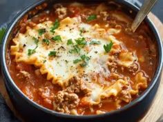 a close up of a bowl of food with pasta and meat in it on a wooden board